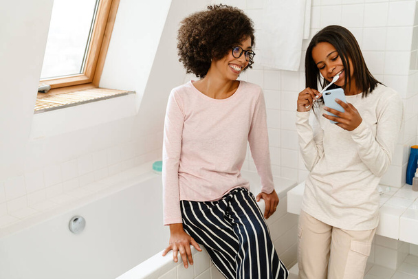 Black girl brushing his teeth and using cellphone in bathroom at home - Foto, Bild