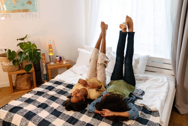 Black girl and her mother laughing and talking while lying on bed at home - Foto, afbeelding