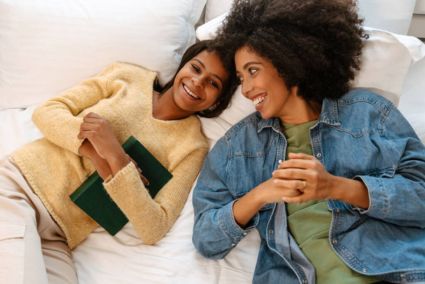zwart meisje en haar moeder lachen en praten terwijl liggend op bed thuis - Foto, afbeelding