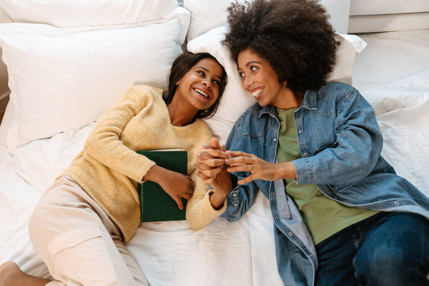 Black girl and her mother laughing and talking while lying on bed at home - Photo, Image