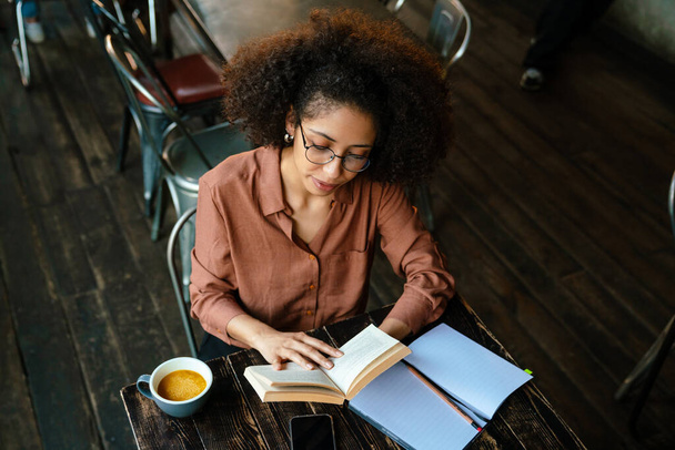 Young black woman with afro hairstyle making notes in planner book in cafe indoors - Foto, imagen