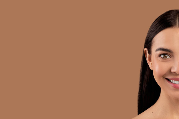 美しいブルネットの髪の長い笑顔の若い女性の半分は、ベージュのスタジオの背景、コピースペースのパノラマに対して完璧な肌で直面しています。美容、顔のケア、審美的な医学の概念 - 写真・画像