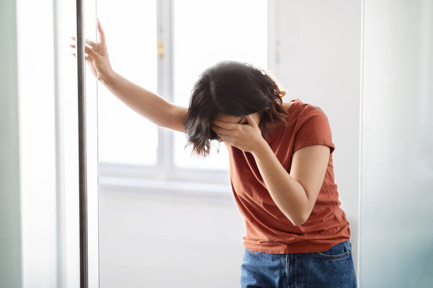 Портрет депресивної молодої жінки, яка плаче біля вікна вдома, міленіалістичне жіноче покриття обличчя з рукою в розпачі, страждання психічного зриву або проблеми з життям, копіювати простір
 - Фото, зображення