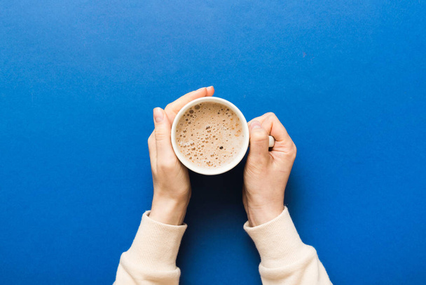 Minimalistinen tyyli nainen käsi pitämällä kuppi kahvia värillinen tausta. Tasainen lay, ylhäältä cappuccino kuppi. Tyhjä paikka tekstille, kopioi tilaa. Kahviriippuvuus. Top view, tasainen lay. - Valokuva, kuva
