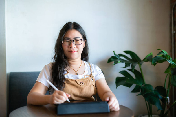 Portrait asian freelance people business female wearing glasses stylish hipste Draw or taking note on digital tablet with electronic pen for browsing internet, chatting and blogging in coffee shop. - Φωτογραφία, εικόνα