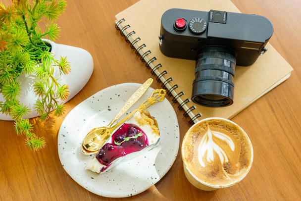 Hot coffee latte with latte art milk foam in cup made of paper and camera in notebook ,Blueberry Cake on wood desk on top view. As breakfast In a coffee shop at the cafe,during business work concept - Foto, Imagem