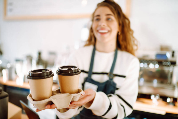 offee to go. Young barista girl smiling happy holding take away coffee at the cafe shop. - Foto, Imagen