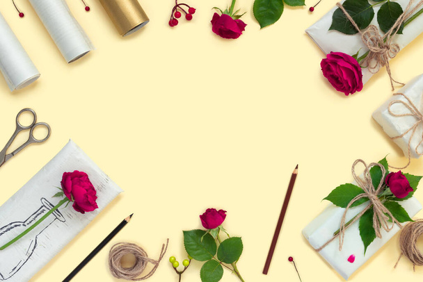 Gifts in paper wrapping, set of vintage yellow package paper, rolls, ropes and pencils for decoration. Bouquet of red roses on yellow vintage background. - 写真・画像