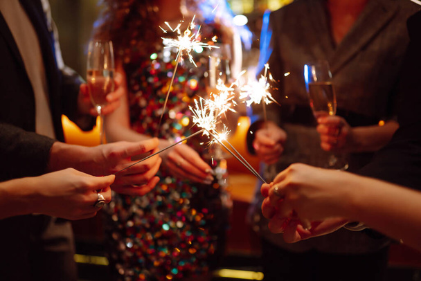 Sparkling sparklers in the hands of friends.Group of people holding sparklers at party. Winter holidays, vacation, relax and lifestyle concept. - Foto, Imagen