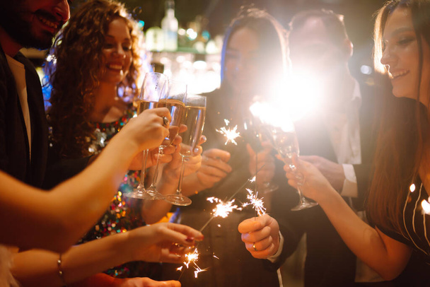 Sparkling sparklers in the hands of friends.Group of people holding sparklers at party. Winter holidays, vacation, relax and lifestyle concept. - Photo, image