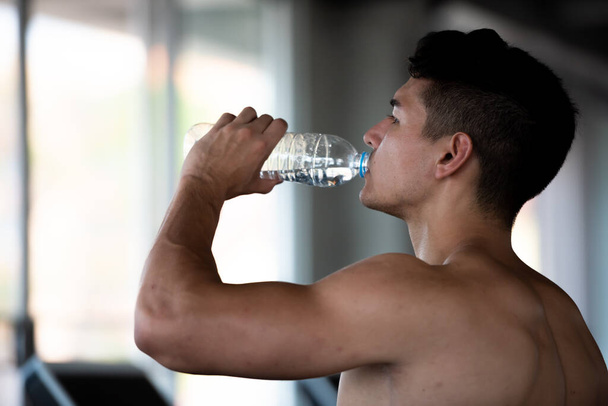 Jeune homme de sport caucasien sain buvant de l'eau dans la salle de sport après l'entraînement. - Photo, image