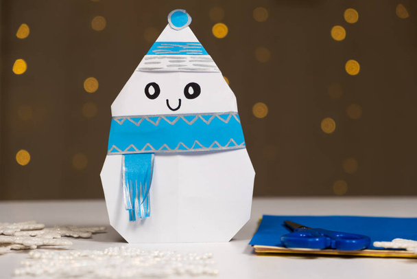 Christmas crafts origami snowman from paper on a background of bokeh, do it yourself. - Photo, Image