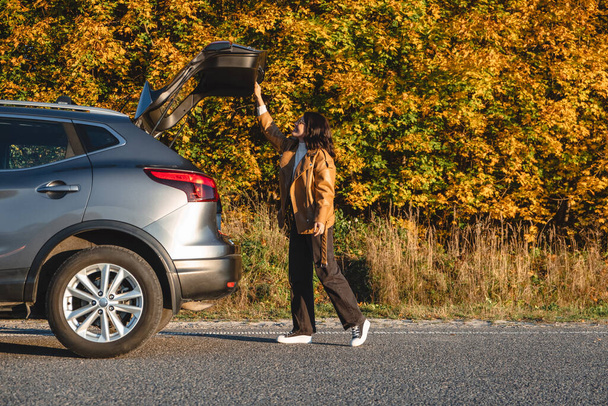 woman closes trunk of car behind autumn forest - Photo, Image