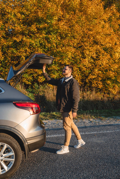 man closes trunk of her car behind autumn forest - Photo, Image