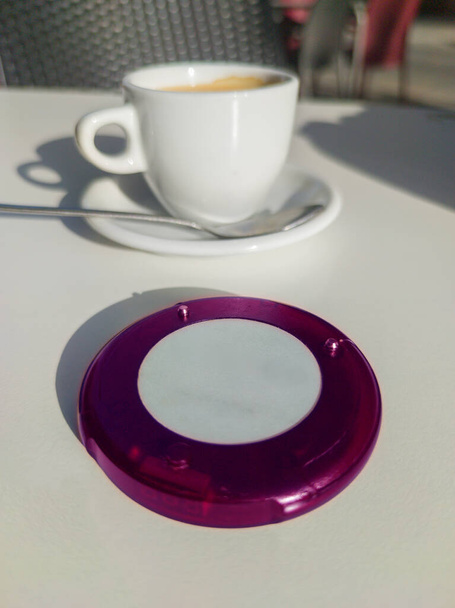 Coaster pager device close to coffee cup at terrace. Wireless communications device for restaurant costumers - Photo, Image