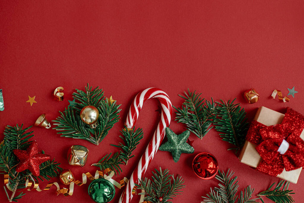 Μοντέρνο Χριστουγεννιάτικο διαμέρισμα. Κομψό χριστουγεννιάτικο δώρο, μπιχλιμπίδια, κλαδιά ελάτης, κομφετί και ζαχαροκάλαμο σε κόκκινο φόντο. Εποχές πρότυπο ευχετήρια κάρτα, χώρος για κείμενο. Χειμερινές διακοπές - Φωτογραφία, εικόνα