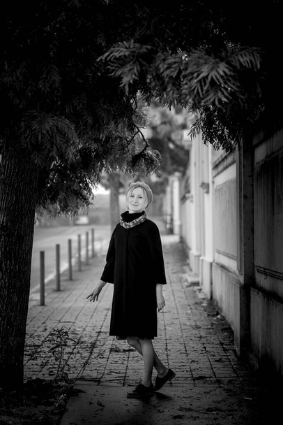 Una mujer con un abrigo de otoño está en la acera. Foto en blanco y negro. - Foto, Imagen