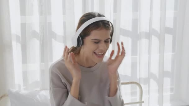 Happy young woman wearing headphones listening music while dancing and singing with fun and enjoy in the living room, happiness female with entertainment, one person, lifestyles concept. - Materiał filmowy, wideo