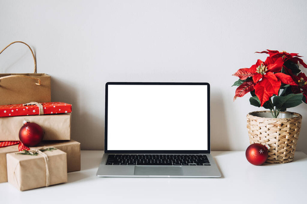 Κενό οθόνη φορητού υπολογιστή οθόνη με Poinsettias Χριστούγεννα Λουλούδι και κουτιά δώρων σε λευκό τραπέζι. Χώρος εργασίας γραφείου στο σπίτι με Mock up χώρο αντιγραφής. Χριστούγεννα online ψώνια, Χειμερινές πωλήσεις - Φωτογραφία, εικόνα