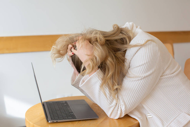 Девушка-фрилансер чувствует усталость и стресс, пользуясь ноутбуком и работая дома. Деловая женщина в офисе в депрессии.  - Фото, изображение