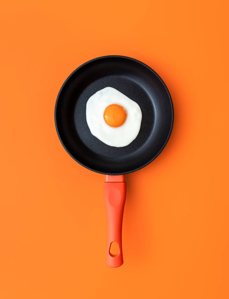 Vue ci-dessus avec un œuf ensoleillé dans une casserole en fonte sur une table de couleur orange. Poêle avec un seul oeuf frit sur un fond coloré. - Photo, image