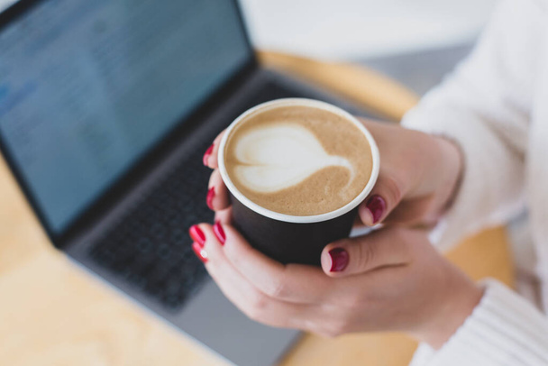 Képek női kézről, amint egy csésze kávét tart a kezében. Kávét elvitelre. A laptop legfelső nézete. Szabadúszó munka. - Fotó, kép