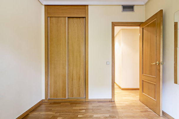 Bedroom in an empty room with a mirror attached to the wall, ducted air conditioning and French oak flooring and an entrance door of the same material and a long corridor with access to other rooms - Photo, Image