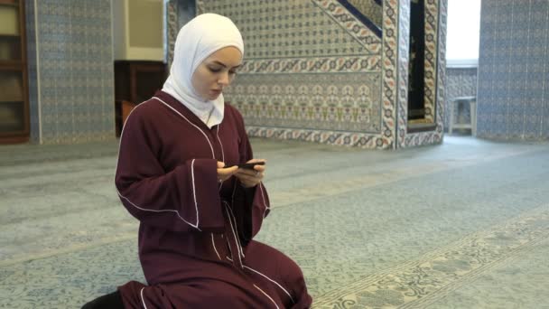 イスラム教徒の女性アプリを使用して、女の子はイスラム教のコンテンツとオンラインプラットフォームを使用して、モスクの電話でクルアーンの朗読に続くアジアの女の子 - 映像、動画