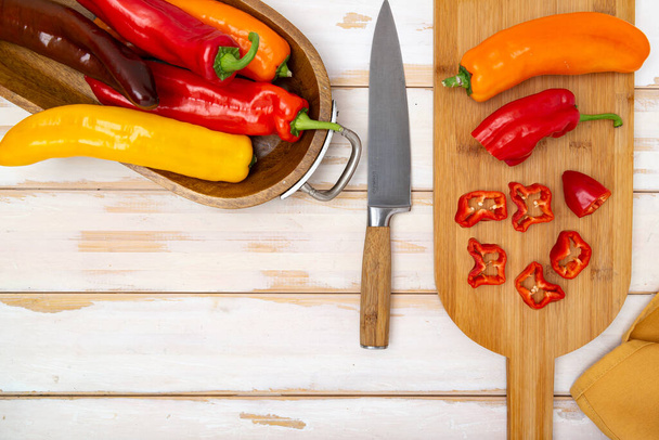 Fresh sweet pepper (bell pepper) on a cutting board with a knife. Chopped pepper pieces are ready to cook. Light wooden table, top view. Space for text. - Fotoğraf, Görsel