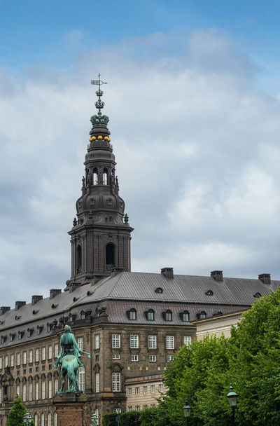 Copenhague, Dinamarca - 23 de julio de 2022: Absalón en su estatua de bronce verde caballo mira el Palacio Christiansborg de piedra gris con su torre y símbolos reales bajo el paisaje nublado azul. Follaje verde - Foto, imagen