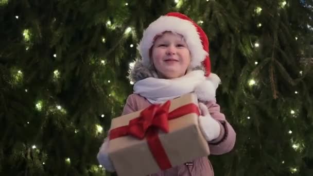 Šťastná holčička v Santa klobouk s vánoční box dárek v zimě venku na Štědrý večer. Vánoční dárky Dovolená dětství koncept - Záběry, video