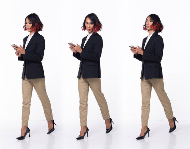 Plná délka 20s asijské žena nosit formální obchodní šaty sako vysoké podpatky boty. Černé krátké kudrnaté vlasy žena chodící šťastný úsměv držet chytrý telefon, jít dopředu vlevo vpravo přes bílé pozadí izolované - Fotografie, Obrázek