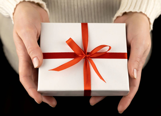 Small white gift box with red ribbon in beautiful female hands - 写真・画像