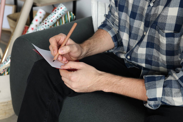 Man writing message in greeting card on sofa in room, closeup - Foto, immagini