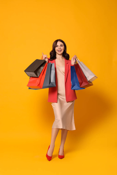 Beautiful young woman with paper shopping bags on yellow background - 写真・画像