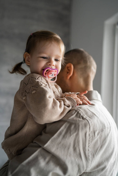 Батько і дочка дорослий білий чоловік тримають свою маленьку дитину маленьку дівчинку біля вікна вдома справжні люди концепція сімейного життя зростаюче місце для копіювання
 - Фото, зображення