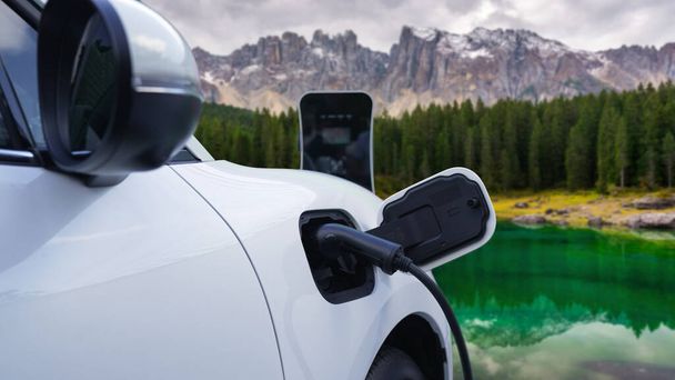 電気発生器ドライブによるエネルギー持続可能な車の電源、プログレッシブ旅行の概念のための山の背景と充電ステーションでバッテリーを充電します。クリーン環境のシンボルとして自然界のEV車. - 写真・画像