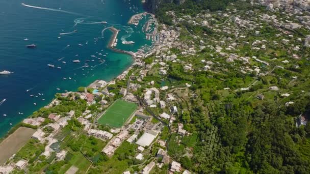 Υψηλή γωνία θέας της ακτής της θάλασσας στον προορισμό των καλοκαιρινών διακοπών. Tilt up αποκαλύπτουν προεξοχή με ψηλά βράχια πάνω από την επιφάνεια του νερού. Capri, Campania, Ιταλία. - Πλάνα, βίντεο