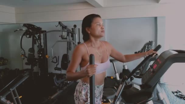 Κοντινό πλάνο μιας νεαρής ταϊλανδέζας γυμναστικής με αθλητικά ρούχα που γυμνάζεται σε καρδιο-μηχανή στο γυμναστήριο, Ασιάτισσες ώριμες γυναίκες μέσης ηλικίας σε εσωτερικούς χώρους στο γυμναστήριο - Πλάνα, βίντεο