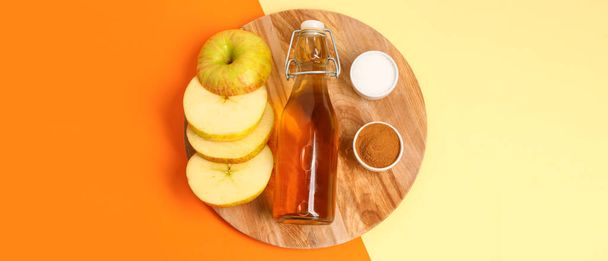 Houten bord met gesneden appel, fles sap, suiker en kaneelpoeder op kleur achtergrond, bovenaanzicht - Foto, afbeelding