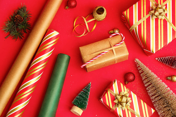 Karácsonyi ajándékok, tekercsek csomagolópapír és dekorációk piros alapon - Fotó, kép