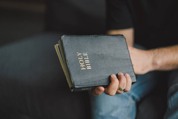 Kristitty mies pitää pyhää Raamattua käsissään. Pyhän Raamatun lukeminen kodissa. Ajatus uskosta, hengellisyydestä ja uskonnosta. Rauha, toivo - Valokuva, kuva