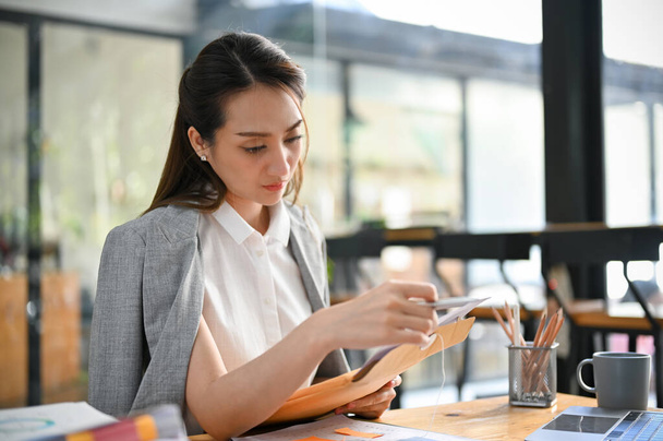 Профессиональная азиатская бизнесвумен или женщина-босс, сосредоточенная на своей работе, чтении письма или документа за своим столом. - Фото, изображение
