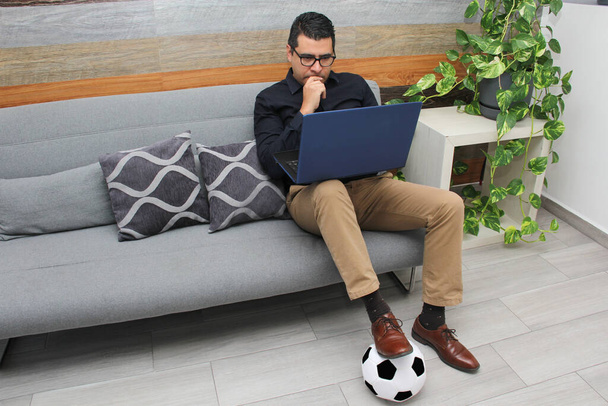 Latino aikuinen toimisto mies katsoo jalkapallo pelejä hänen työpöydällään työaikana aamulla, hän näkee hänet hermostunut, surullinen, stressaantunut, vihainen vieressä hänen jalkapallo pallo - Valokuva, kuva