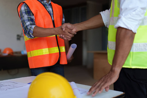 Arquitecto e ingeniero trabajadores de la construcción estrechando la mano después de terminar un acuerdo en el sitio de construcción de oficinas, concepto de colaboración de éxito. - Foto, imagen