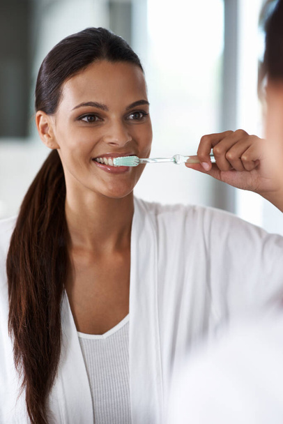 Bereiten Sie sich auf den Tag vor. eine lächelnde junge Frau beim Zähneputzen im Spiegel - Foto, Bild