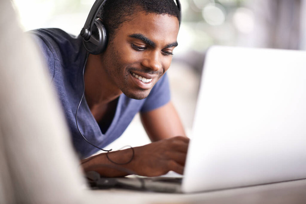 Relaksuje się podczas nauki. przystojny młody mężczyzna korzystający z jego laptopa podczas relaksu w domu - Zdjęcie, obraz