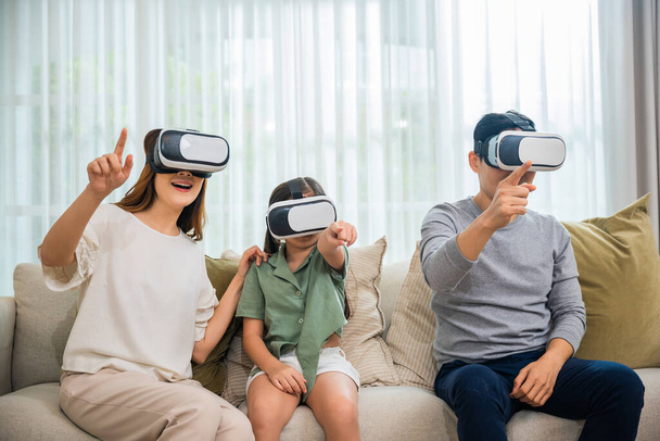 Happy family have mother father and daughter watching movie or playing video game, Asian family wear vr glasses headsets fun sitting on sofa in living room, game entertainment innovation technology - Фото, зображення