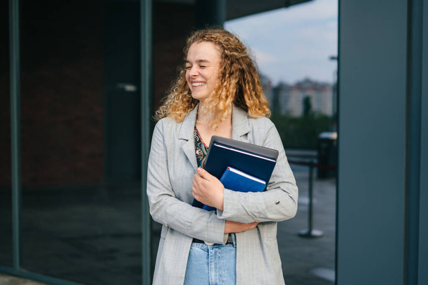 Portret van een jonge studente met boeken en laptop van de universiteit na de les, lopend op straat. Het concept van mens en stedelijke levensstijl - Foto, afbeelding