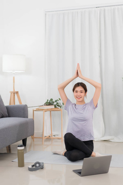 Yoga exercise concept, Asian woman raising arms over head in lotus position while doing yoga online. - Фото, зображення